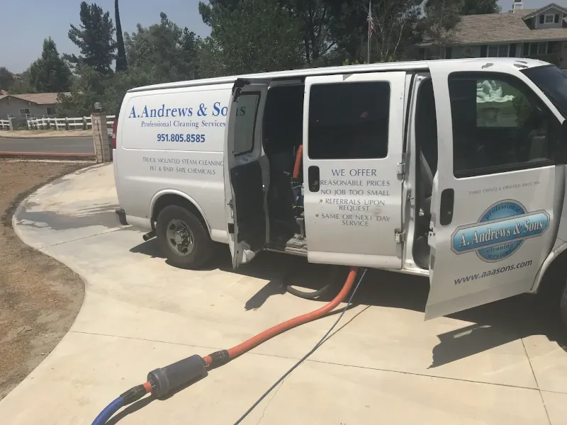 White cleaning service van with open doors and a hose extending from inside onto a driveway.