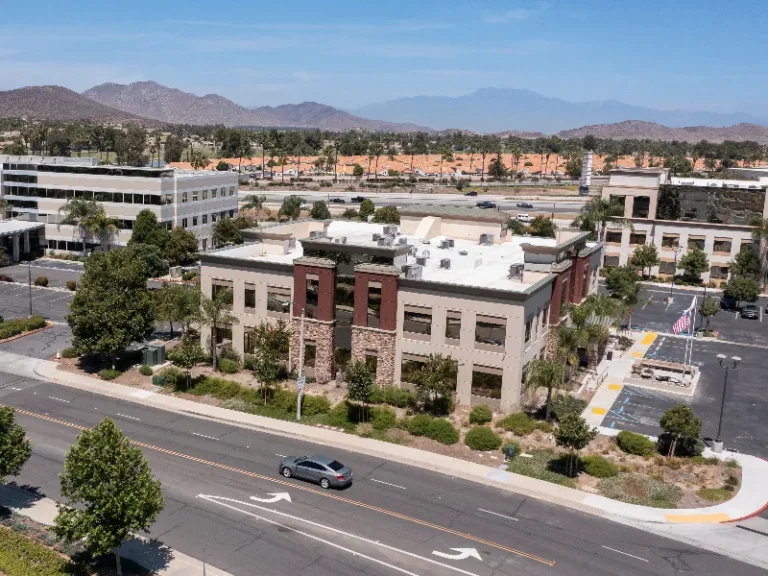 Office buildings with parking lots near a highway and mountains in the background.