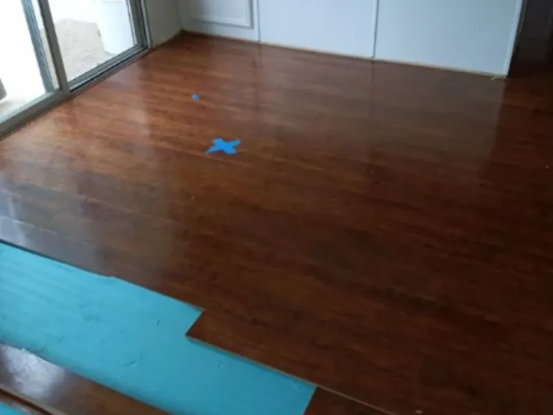 Partially installed wooden floor with blue underlayment and blue tape markings.