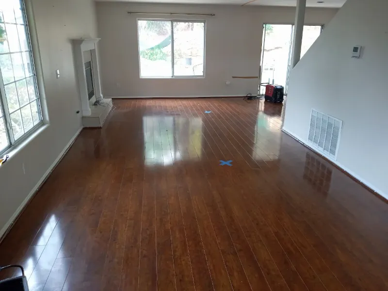 Empty room with polished wooden floor, large windows, and a fireplace on the left wall.