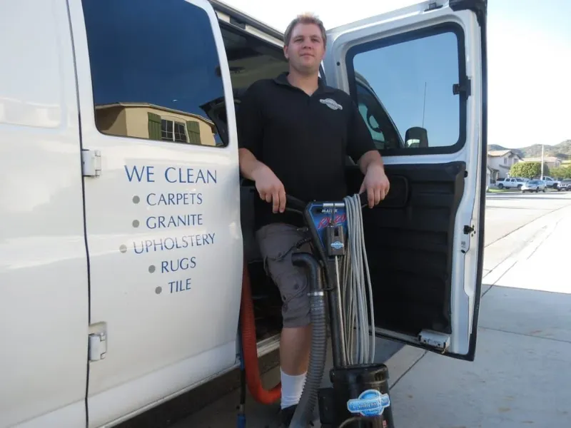 Man standing with carpet cleaning machine next to an open van door with cleaning service list on the van.