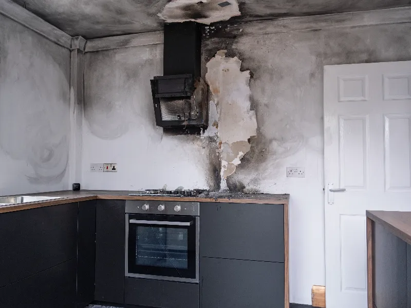 Kitchen wall and ceiling damaged by fire and smoke around a stove and extractor hood.