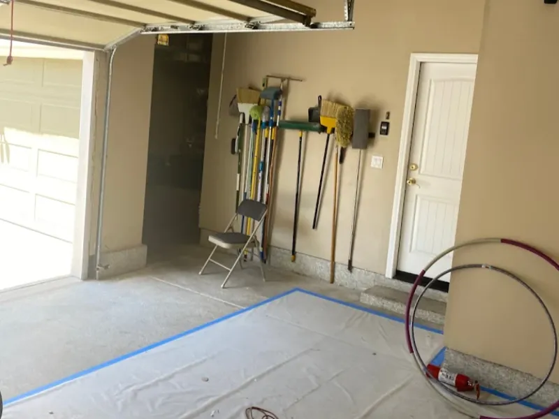 Garage corner with cleaning tools hanging on the wall, a folding chair, and hula hoops on the floor.