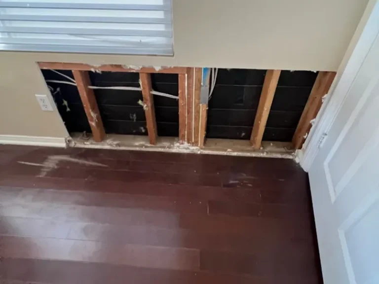 Section of wall drywall removed exposing wooden studs and wiring behind it.