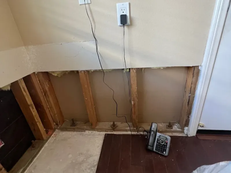 Wall with lower drywall removed exposing wooden studs and a cordless phone on the floor.