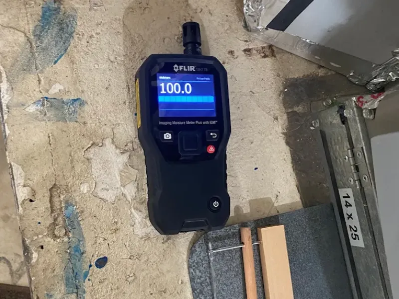Moisture meter displaying a reading of 100.0 on a rough, stained surface.