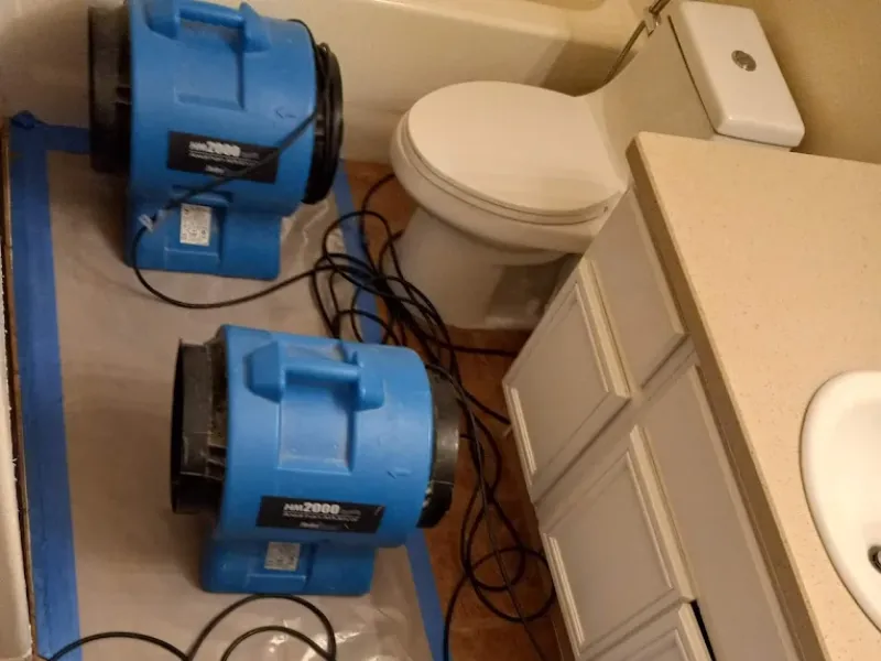 Two blue air movers placed on a bathroom floor near a toilet and vanity.